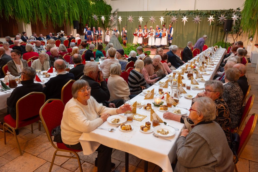 goście siedzą przy zastawionych stołach na atrium Centrum Kultury Wsi Polskiej w Wierzchosławicach a w tle widoczny śpiewający Zespół Pieśni i Tańca Swojacy w tradycyjnych strojac