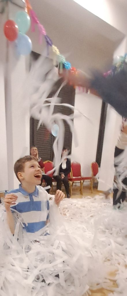 ozdobiona balonami i girlandami sala balowa a pośrodku dzieci rzucające ogromnym confetti