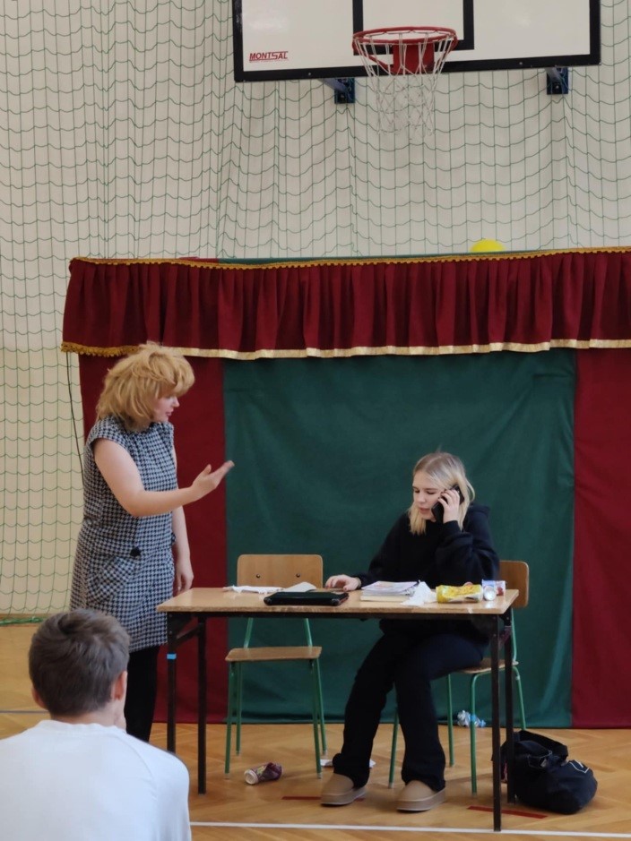 nauczyciel rozmawia z uczniem siedzącym w szkolnej ławce