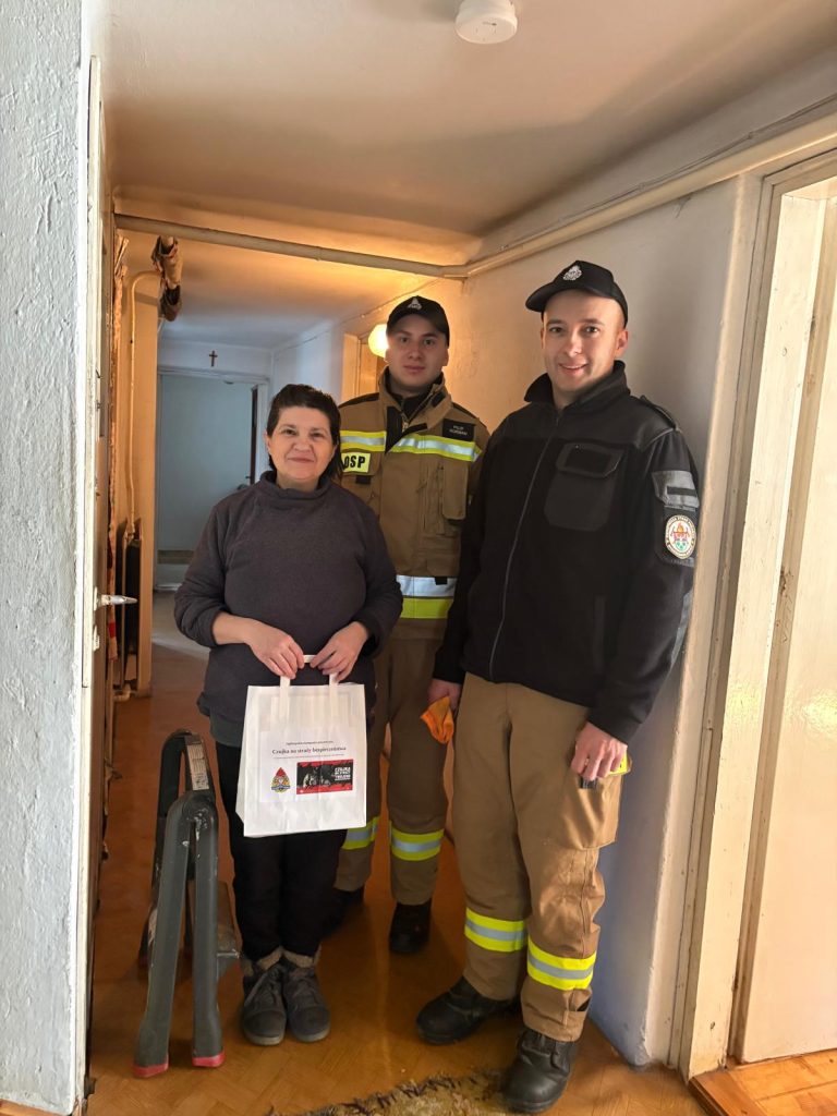 Dwóch strażaków i kobieta trzymająca w ręku torbę z napisem Czujka na straży bezpieczeństwa