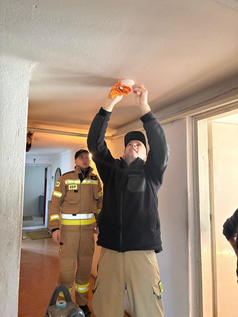 stażacy montują czujkę dymu na suficie pokoju